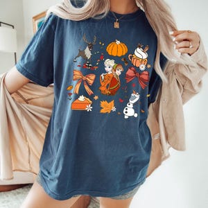 May include: Navy blue t-shirt with a colorful fall-themed graphic. The design includes a reindeer, pumpkin, pie, and cartoon characters. The word "Midnight" is printed at the top left of the shirt.
