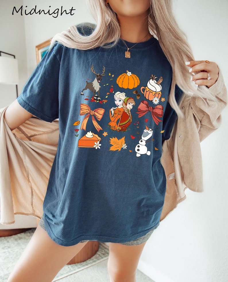 May include: Navy blue t-shirt with a colorful fall-themed graphic. The design includes a reindeer, pumpkin, pie, and cartoon characters. The word "Midnight" is printed at the top left of the shirt.
