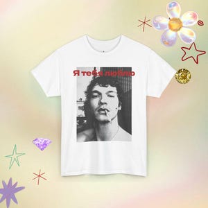 May include: A white short-sleeved t-shirt featuring a black and white photographic print of a person with a cigarette in their mouth. Above the portrait, the red Cyrillic text "Я тебя люблю" is printed. The shirt has a crew neckline.