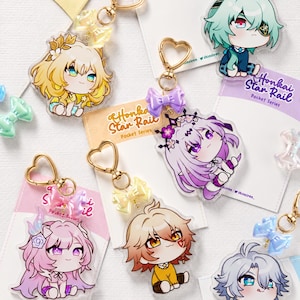 May include: Collection of acrylic keychains featuring anime-style characters. Each keychain has a gold heart-shaped clasp and a colorful bow accent. The keychains are on cards that say "Honkai Star Rail Pocket Series."