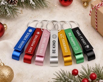 May include: A set of seven metal bottle openers in blue, red, pink, silver, gold, green, and black. Each opener features a silver ring and white text: GOOD VIBES, STAY POSITIVE, YOU GOT THIS, BE KIND, CHEERS, BE HAPPY, and TAKE IT EASY with icons.