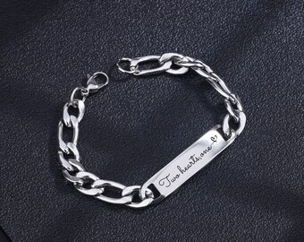 May include: A silver-colored bracelet with a chain link design. The bracelet features a rectangular plate engraved with the words "Two hearts, one" and a small heart symbol. The bracelet is displayed on a black surface.