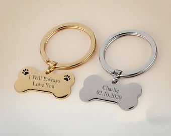 May include: Two dog bone-shaped pet ID tags. One is gold-colored with the text "I Will Paways Love You" and paw prints. The other is silver-colored with the name "Charlie" and the date "02.10.2020". Both have a metal ring.