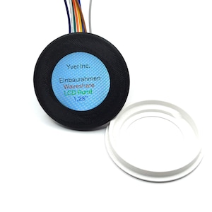 May include: A black round LCD display bezel with a blue and green label that reads "Yver Inc. Einbaurahmen Waveshare LCD Rund 1,28" ". The bezel is separated from a white plastic ring.