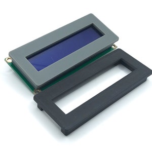 Op de afbeelding: Een grijs en zwart plastic frame voor een klein LCD-scherm. Het frame is ontworpen om een ​​16x2-karakters LCD-scherm te bevatten.
