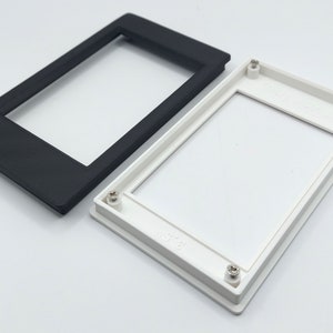 May include: Two plastic frames for a small electronic device. One frame is black and the other is white. Both frames have four screw holes.