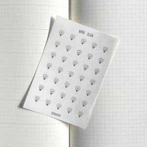Puede incluir: Una hoja de pegatinas con un icono de bombilla repetido varias veces. La hoja es blanca con texto negro que dice "MINI ICON" y "FREMON".