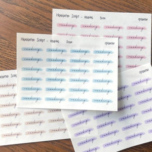Puede incluir: Cuatro hojas de pegatinas con la palabra "lectura" escrita en cursiva en cada pegatina. Las pegatinas son de cuatro colores diferentes: rosa blush, azul océano, azul claro y lavanda. Cada hoja tiene las palabras "HIGHLIGHTED SCRIPT - READING" en la parte superior.