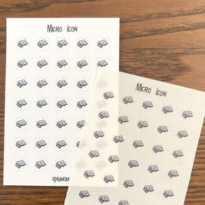 May include: Two sheets of clear sticker paper with a repeating pattern of small black book icons. The text "MICRO ICON" is written at the top of each sheet. The text "OPIGMOM" is written at the bottom of each sheet.