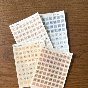 May include: Four sheets of date stickers with different color backgrounds and designs. Each sheet has a title and numbers 1 through 31. The colors are dusty blue, peach, beige, and light brown.