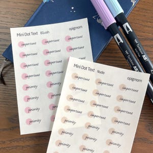 May include: Two sheets of stickers with the text "Mini Dot Text Blush" and "Mini Dot Text Nude" featuring the words "important" and "priority" in black script. The stickers have pink and nude-colored dots. Two Tombow ABT markers and a blue notebook are also visible.