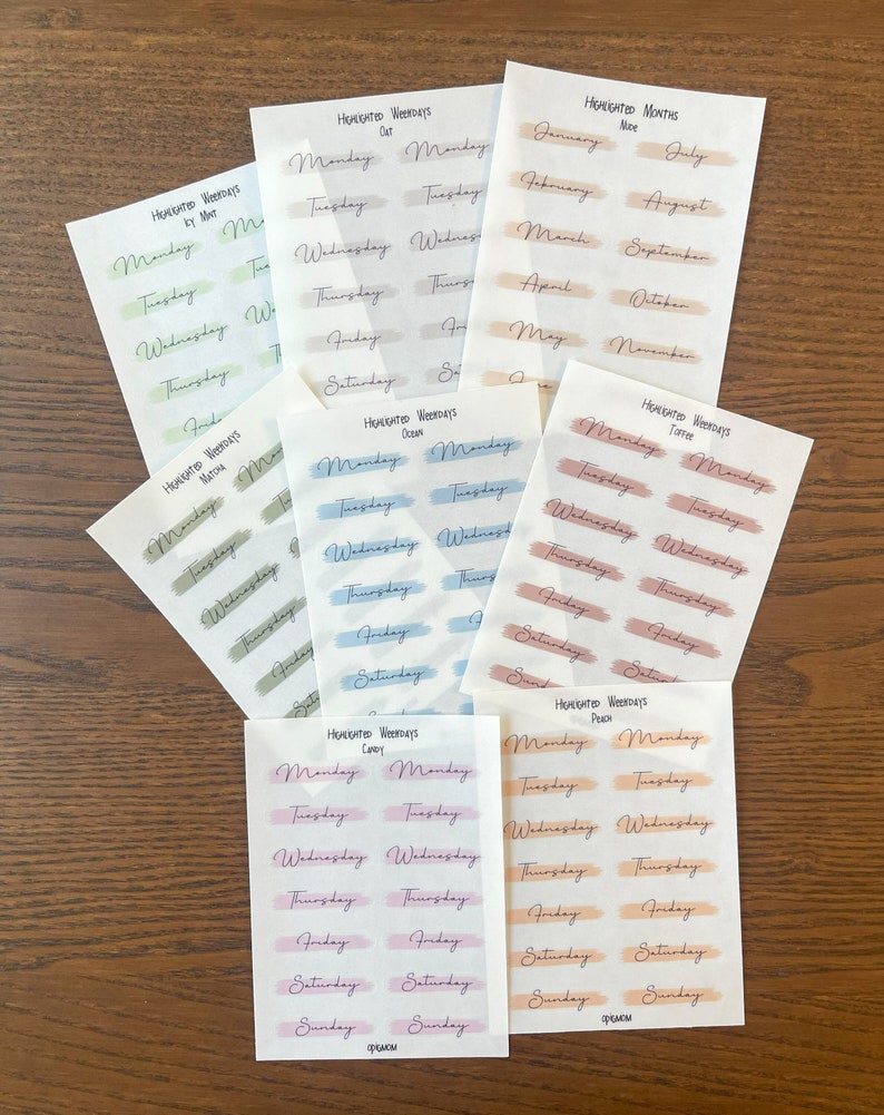 May include: A set of 10 sheets of clear stickers with handwritten days of the week and months of the year. Each sticker has a watercolor-style wash of color in a different shade of blue, green, pink, or orange.