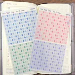 Puede incluir: Cuatro hojas de cinta washi estampada. La hoja superior es azul y verde, la segunda hoja es rosa y morada, la tercera hoja es azul y verde, y la cuarta hoja es azul y morada. La cinta washi está etiquetada como "Thick Washi Strip" y "Opigmom".