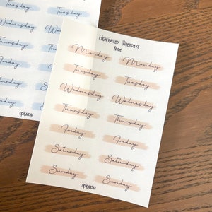 May include: Two sheets of stickers with the days of the week written in cursive. The top sheet has the days of the week in blue and white, while the bottom sheet has the days of the week in peach and white.
