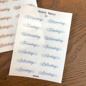 May include: A sheet of stickers with the days of the week written in cursive. The stickers are in two colors: light blue and light pink. The text "HIGHLIGHTED WEEKDAYS" is printed at the top of the sheet.