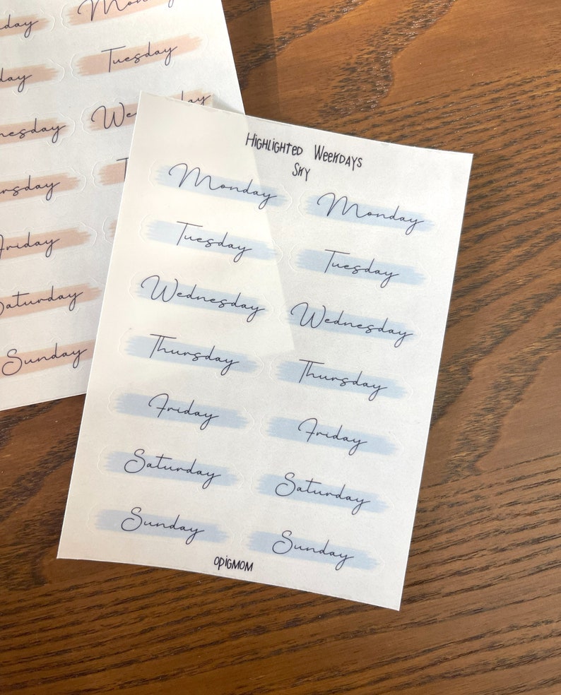 May include: A sheet of stickers with the days of the week written in cursive. The stickers are in two colors: light blue and light pink. The text "HIGHLIGHTED WEEKDAYS" is printed at the top of the sheet.