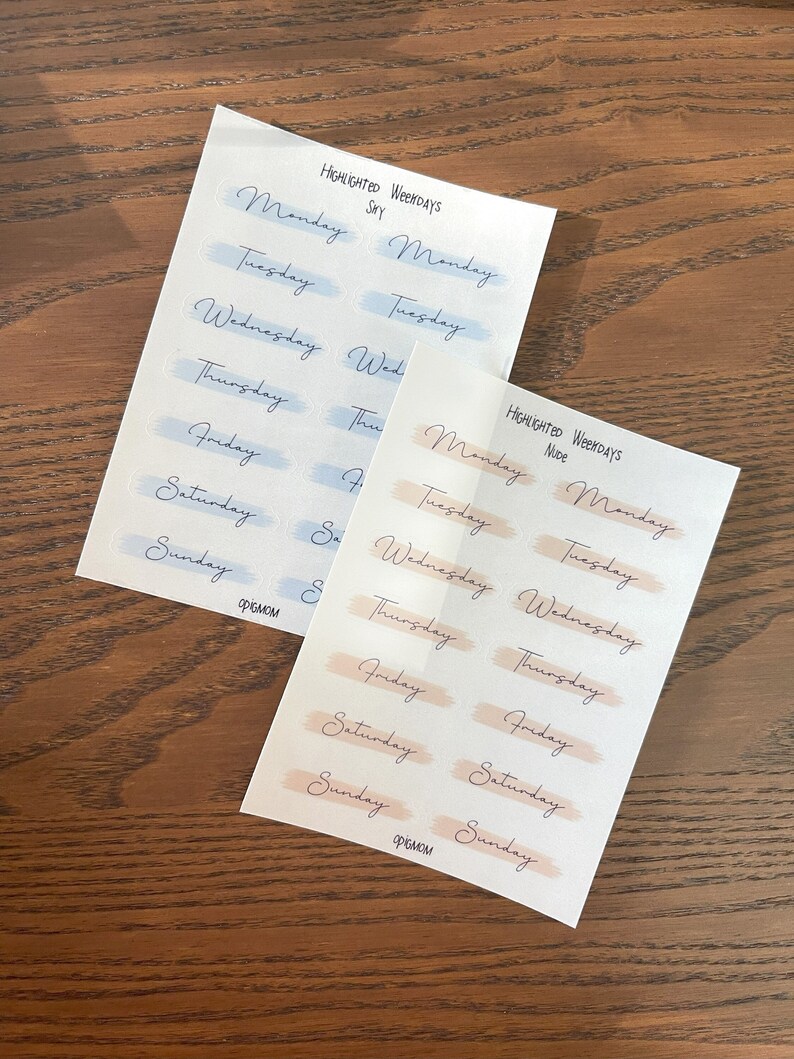 May include: Two sheets of stickers with the days of the week written on them. The top sheet has a blue watercolor background and the bottom sheet has a peach watercolor background. The text on the stickers reads "HIGHLIGHTED WEEKDAYS" and "Sky" on the top sheet and "HIGHLIGHTED WEEKDAYS" and "Nude" on the bottom sheet.