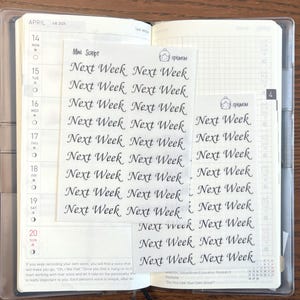 May include: A close-up of a planner with a clear plastic cover. The planner is open to the month of April and has a gridded page for daily notes. There are several stickers on the page that say "Next Week" in cursive writing.