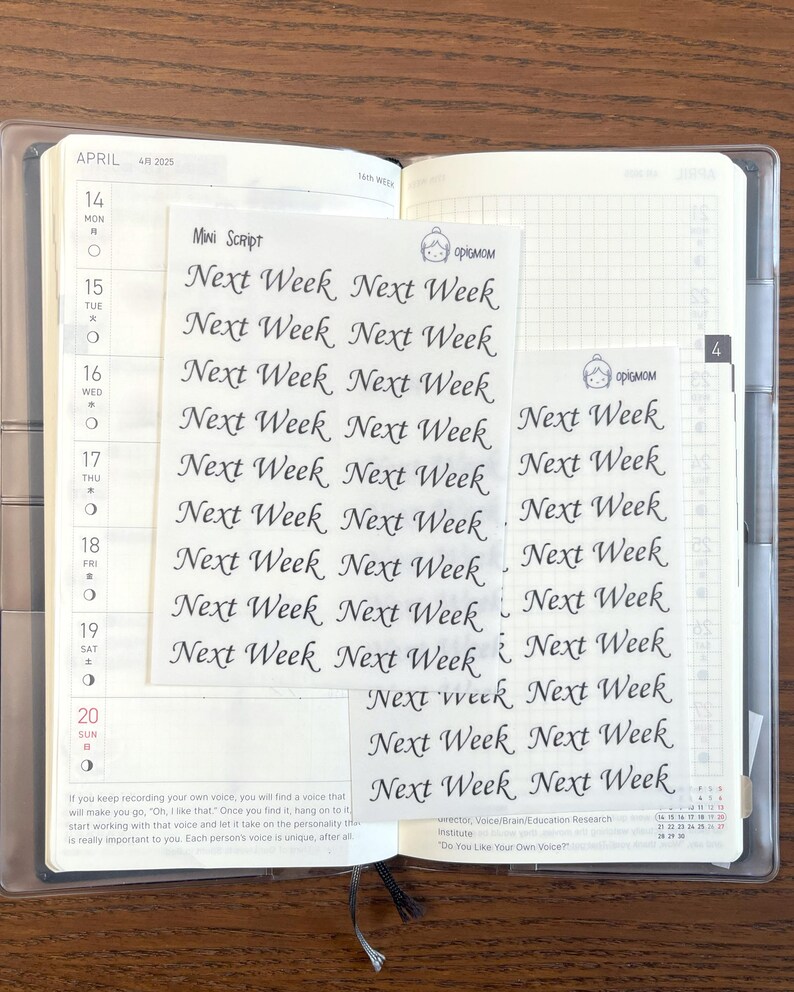 May include: A close-up of a planner with a clear plastic cover. The planner is open to the month of April and has a gridded page for daily notes. There are several stickers on the page that say "Next Week" in cursive writing.