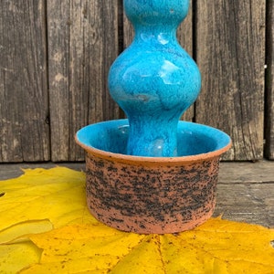 Peut inclure: Un bougeoir en céramique bleu turquoise avec une base ronde et une finition texturée. Le bougeoir a un design unique avec une petite ouverture ronde en haut.