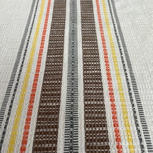 May include: White kitchen towel with brown, grey, orange and yellow stripes.