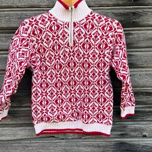 May include: A red and white patterned sweater with a half-zip closure. The sweater has a mock neck and long sleeves.