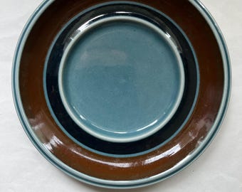 May include: A ceramic plate with a teal center, surrounded by concentric rings of black, brown, and teal. The plate has a glossy finish and a simple, modern design. This plate is suitable for serving food.