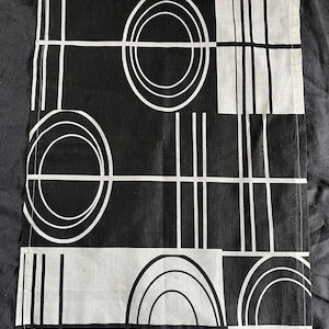 Puede incluir: Tela negra y blanca con un patrón geométrico de círculos y líneas. La tela tiene un brillo sutil y una textura suave.