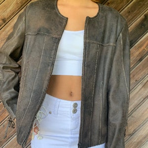 Könnte beinhalten: Eine braune Lederjacke mit Reißverschluss und weißen Nähten. Die Jacke hat einen runden Ausschnitt und lange Ärmel.