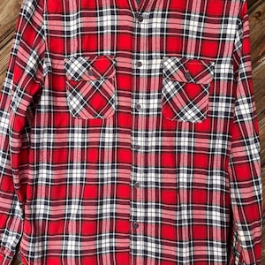 May include: Red, white, and blue plaid long-sleeve button-up shirt. The shirt has two chest pockets and a button-down collar.
