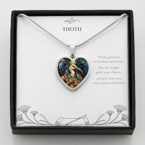 May include: A silver heart-shaped pendant necklace featuring an illustration of the Egyptian deity Thoth. The card displays the text THOTH, Thoth, guardian of wisdom and words. May his insight guide your choices, and give your own voice room to be heard.