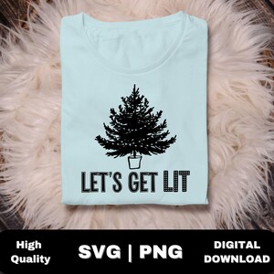 以下が含まれることがあります： 薄い青色のTシャツに、黒いシルエットのクリスマスツリーとライト、そして黒い文字で「Let's Get Lit」と書かれています。