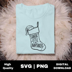 Puede incluir: Una camiseta azul claro con una ilustración en blanco y negro de una media con un bebé durmiendo dentro. La media tiene el texto "Santa's Little Naptaker".