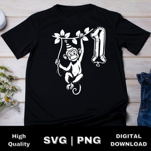May include: Black t-shirt with a white graphic of a monkey wearing a party hat and holding a number one balloon. The monkey is hanging from a vine.