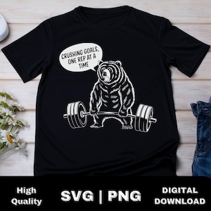 May include: Black t-shirt with a white graphic of a bear lifting weights. The text "Crushing Goals, One Rep at a Time" is above the bear.