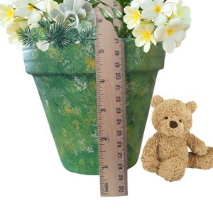 May include: A green and yellow speckled terracotta pot with white flowers and a green plant inside. The pot is 7 inches tall and is next to a teddy bear.