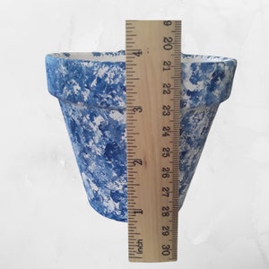 May include: A blue and white glazed terracotta planter pot, approximately 6 inches tall, measured against a ruler.