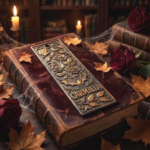 May include: A bronze bookmark with floral and bat designs, and the word "CARMILLA" is placed on a vintage book with a burgundy cover. The scene includes autumn leaves, roses, and lit candles, creating a gothic aesthetic.