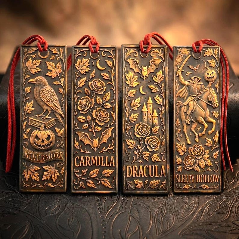 May include: Four bronze-colored rectangular bookmarks with red cords. Each bookmark features a different embossed design: a raven, roses and bats, a castle, and a headless horseman. The bookmarks have the words "Nevermore", "Carmilla", "Dracula", and "Sleepy Hollow".