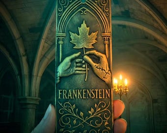 May include: A rectangular, bronze-colored plaque with the word "FRANKENSTEIN" in white lettering. The plaque features a relief of two hands holding a maple leaf. The background is a gothic-style interior with arched ceilings and candlelight.