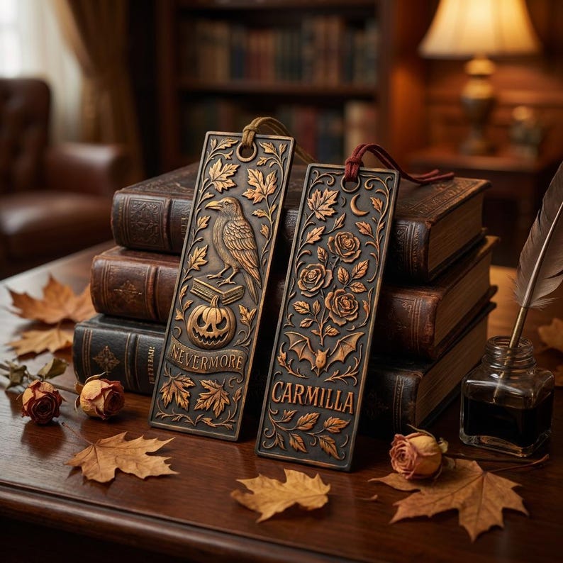 May include: Two ornate metal bookmarks with embossed designs rest on a stack of books. One features a raven, pumpkin, and the word "Nevermore." The other displays roses, a bat, and the word "Carmilla." Autumn leaves and dried roses decorate the table.