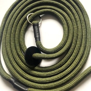 May include: Olive green dog lead made of braided rope, coiled in a circular pattern. The lead features a black handle and a silver metal ring for attachment. The rope is thick and durable, suitable for medium to large dogs.
