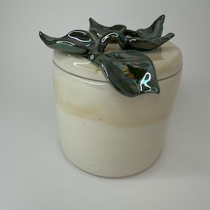 Puede incluir: Jarrón de cerámica blanco con una tapa con un diseño floral verde iridiscente.