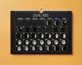 May include: A black wall calendar for January with white text and a grid layout. Each day features a realistic illustration of the moon phase. Small gold shooting star icons appear on the 3rd and 5th. The calendar is held by a silver wire spiral.