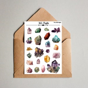 May include: A white sticker sheet featuring various colorful crystal illustrations, including amethyst, citrine, and quartz clusters. The top of the sheet displays the text 365 Nights and The 008 Night. The sheet is placed on a brown paper envelope.