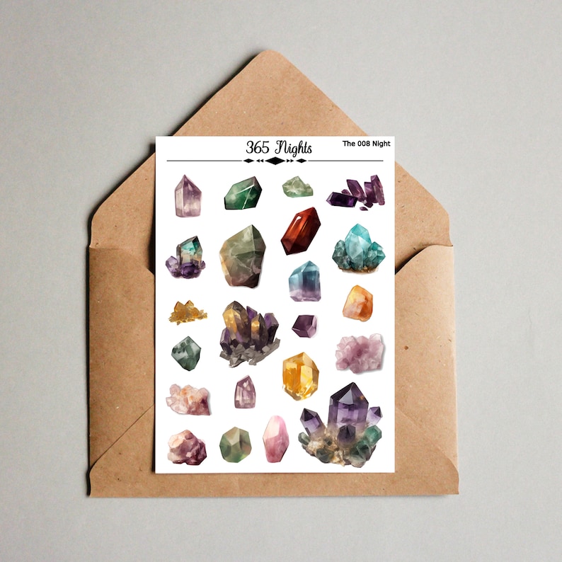 May include: A white sticker sheet featuring various colorful crystal illustrations, including amethyst, citrine, and quartz clusters. The top of the sheet displays the text 365 Nights and The 008 Night. The sheet is placed on a brown paper envelope.