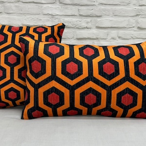 May include: Two decorative throw pillows with a geometric pattern in black, orange, and red. The pattern resembles a honeycomb or a maze.