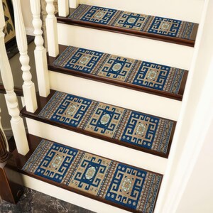 Può includere: Scala con quattro gradini, ognuno adornato da un tappeto rettangolare. I tappeti presentano un motivo geometrico ripetuto nelle tonalità del blu, beige e marrone. La scala ha alzatine bianche e gradini marrone scuro.