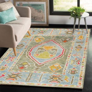 Könnte beinhalten: Ein grüner, blauer und orangefarbener Teppich mit geometrischem Muster. Der Teppich hat einen hellblauen Hintergrund mit einer zentralen grünen Raute.