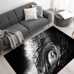 May include: Black and white abstract rug with a wave design. The rug has a white splash of water on the left side and a black wave on the right side.